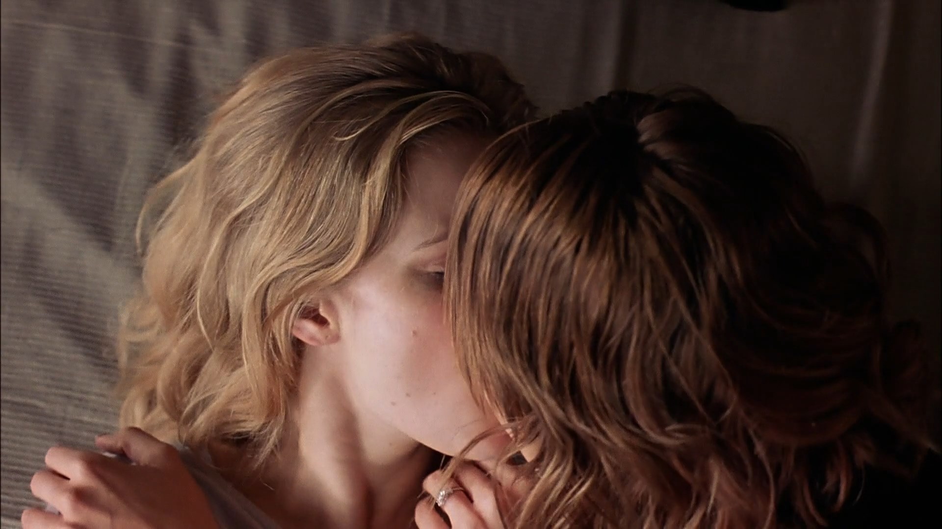 Amy Adams and Lauren German sit on a bed and kiss. 